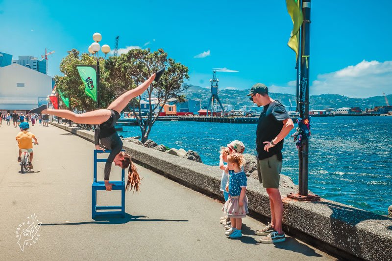 woman does acrobats on a chair in front of small crowd by the sea