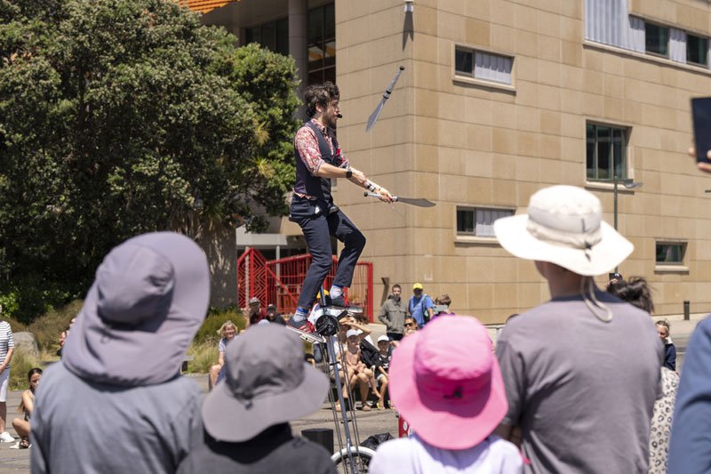 man juggles knives on unicycle while crowds stand around
